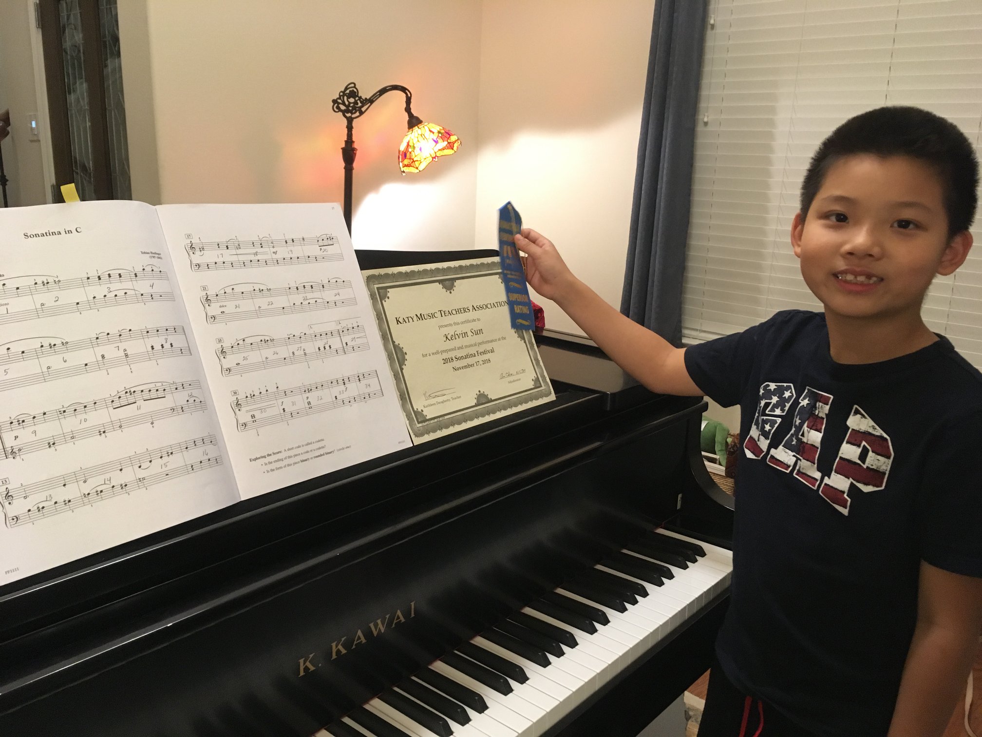 Boy stands by grand piano with blue ribbon and an award.