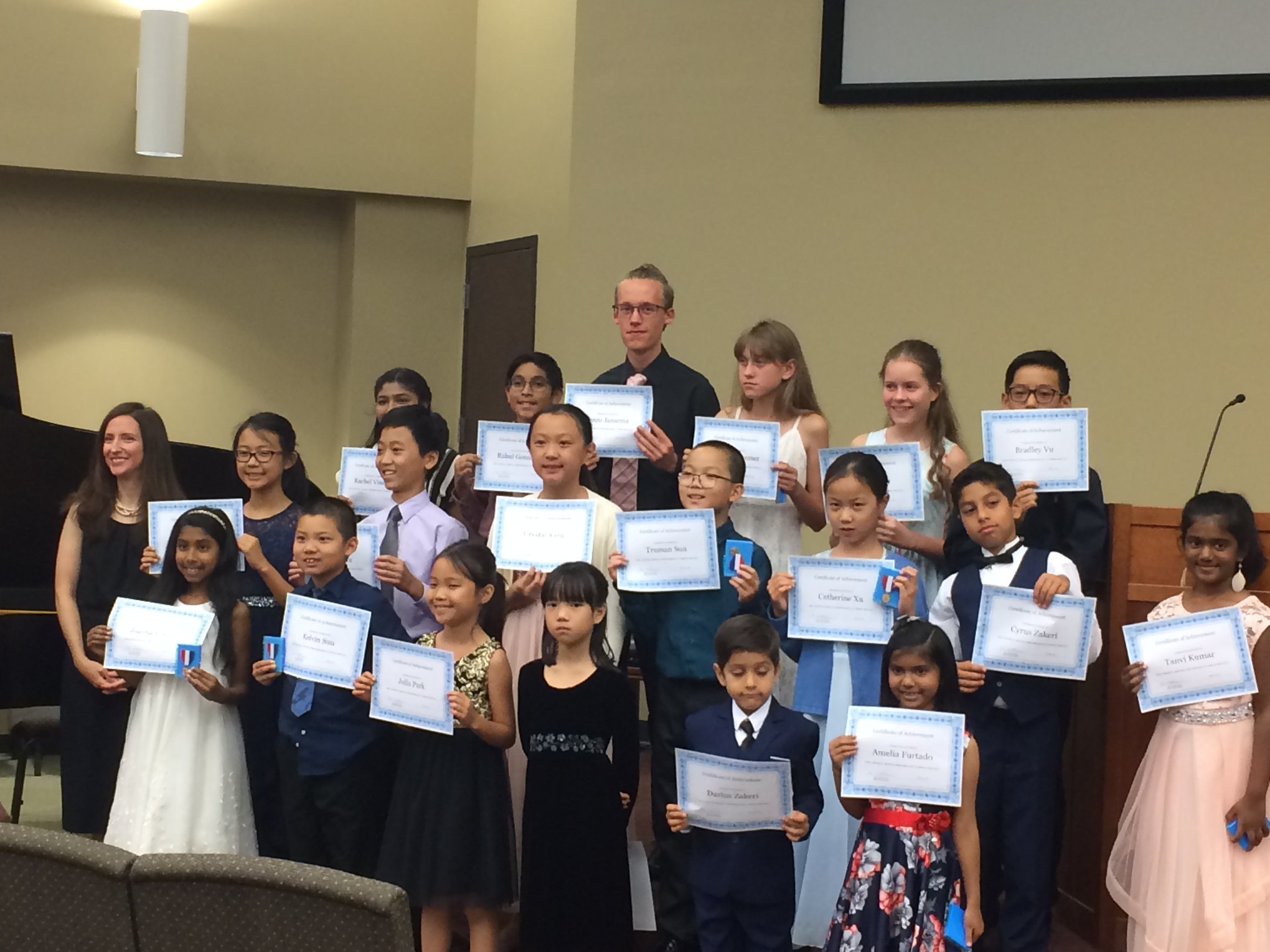 Students pose for a group photo holding certificates after a recital.