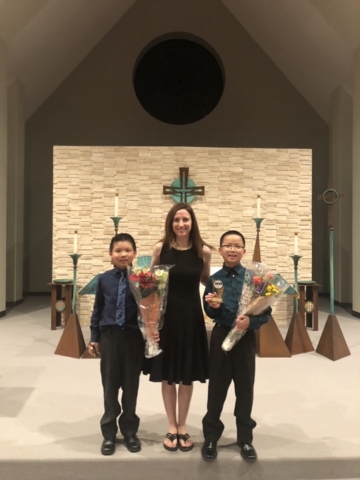 Ms. Kathleen stands with two brothers holding flowers and trophies.