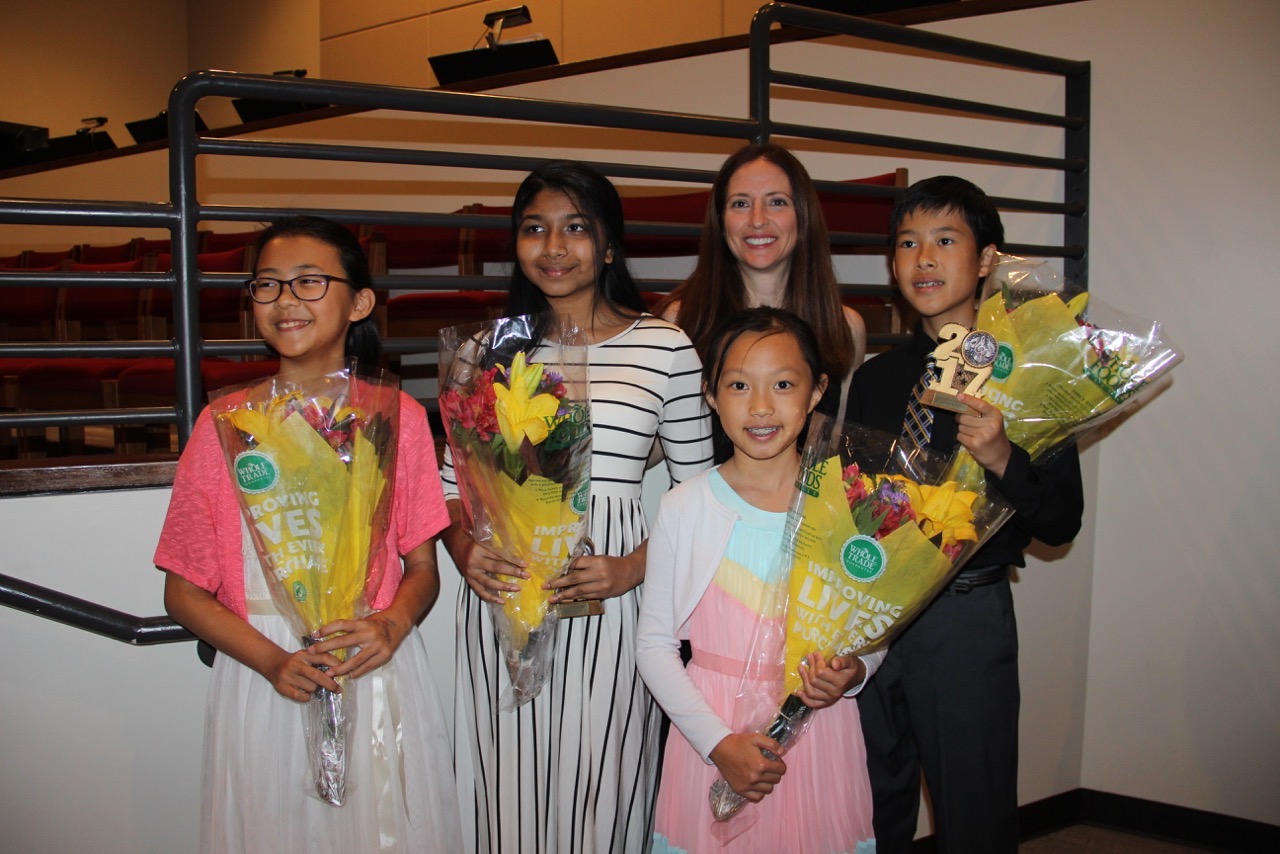 Four middle school and high school students smile holding flowers after a performance.
