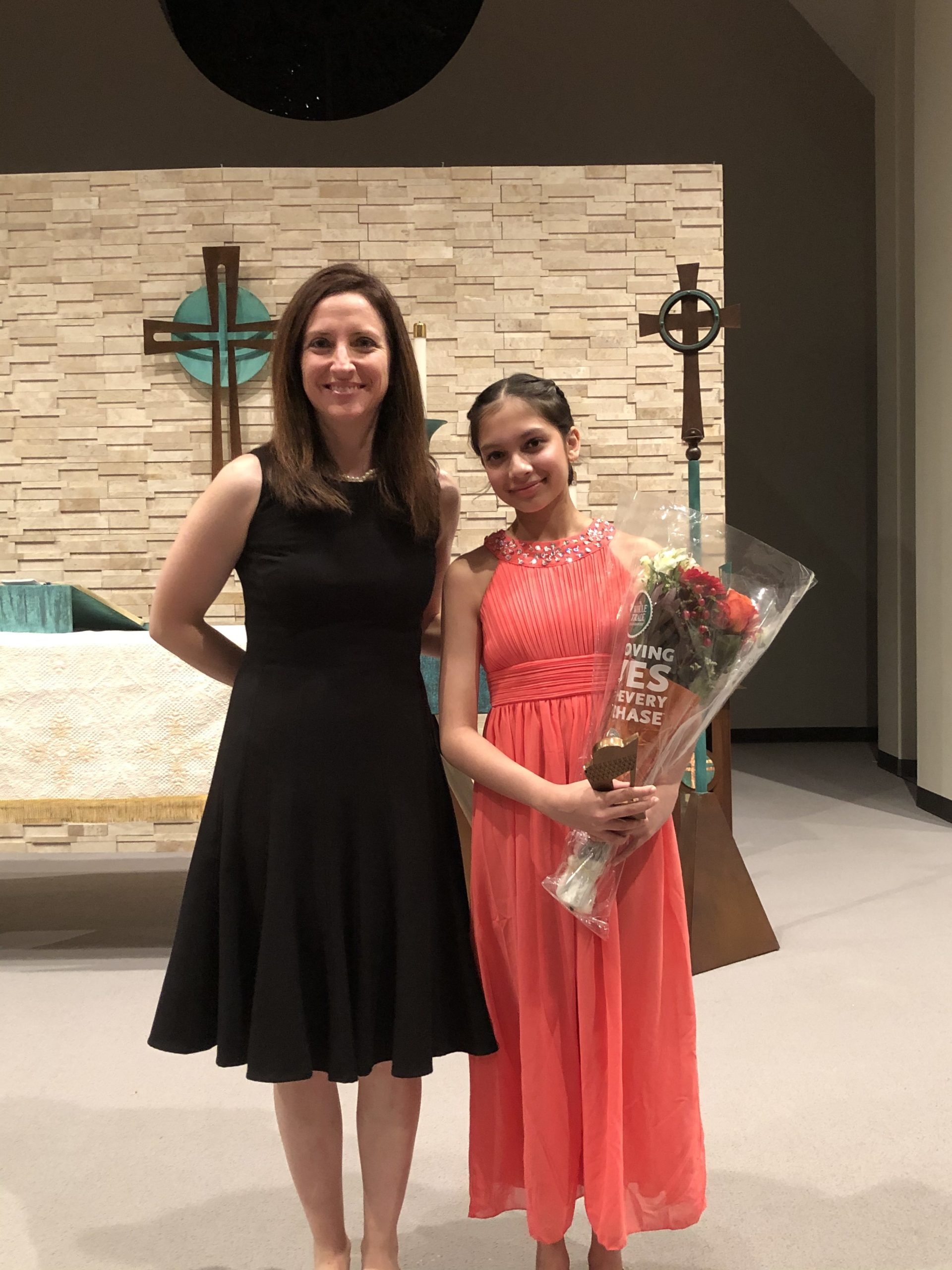 Girl in a long orange dress stands with her teacher.
